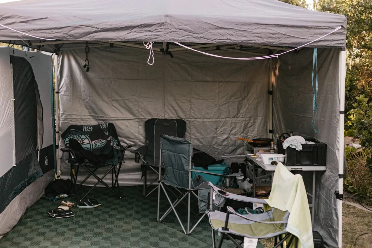 A gray pop-up canopy with sidewalls set up over camping chairs and a camp kitchen A gray pop-up canopy with sidewalls set up over camping chairs and a camp kitchen