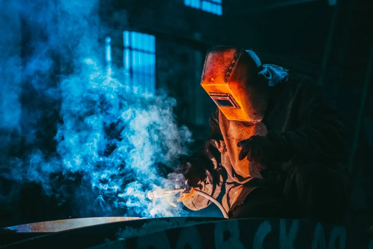 A welder in a protective mask working in a smoky workshop A welder in a protective mask working in a smoky workshop