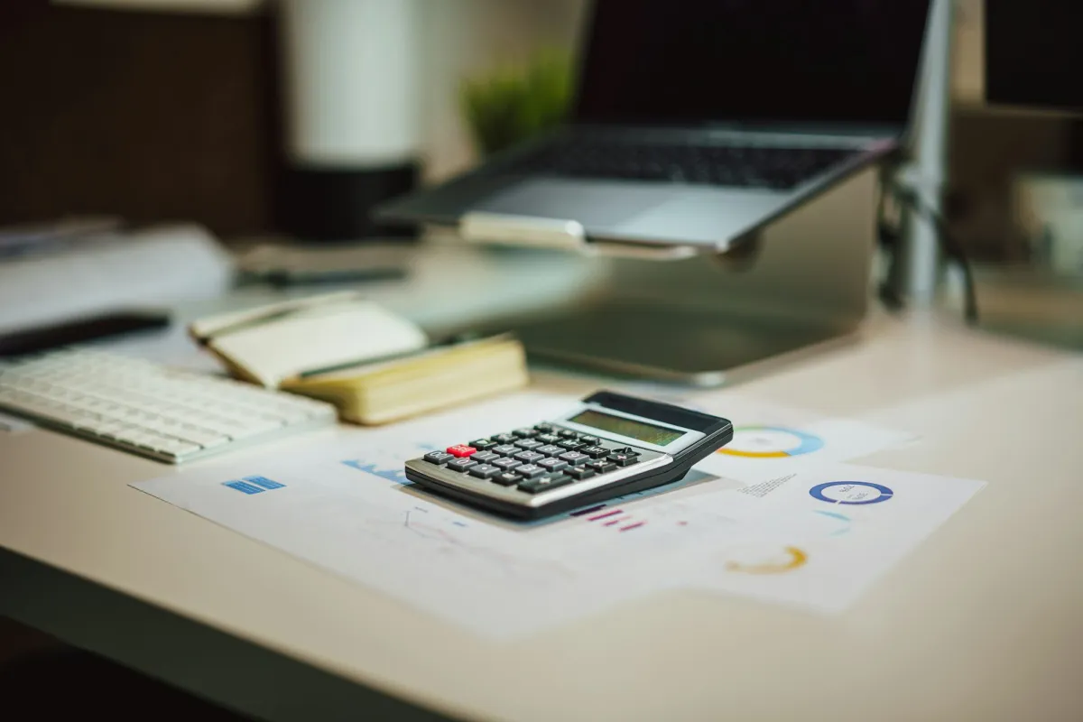A calculator on printed charts on a desk, with a laptop and keyboard behind it A calculator on printed charts on a desk, with a laptop and keyboard behind it