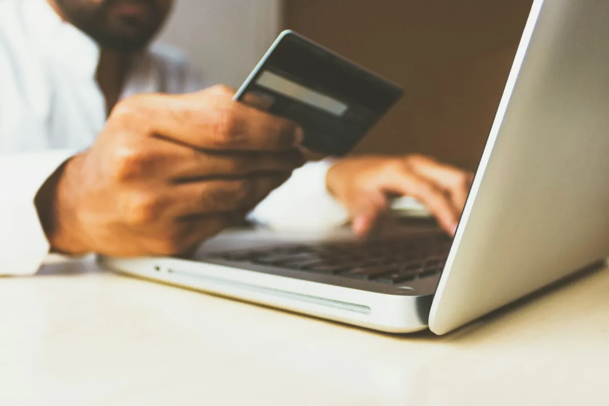 A person holding a payment card while typing on a laptop A person holding a payment card while typing on a laptop