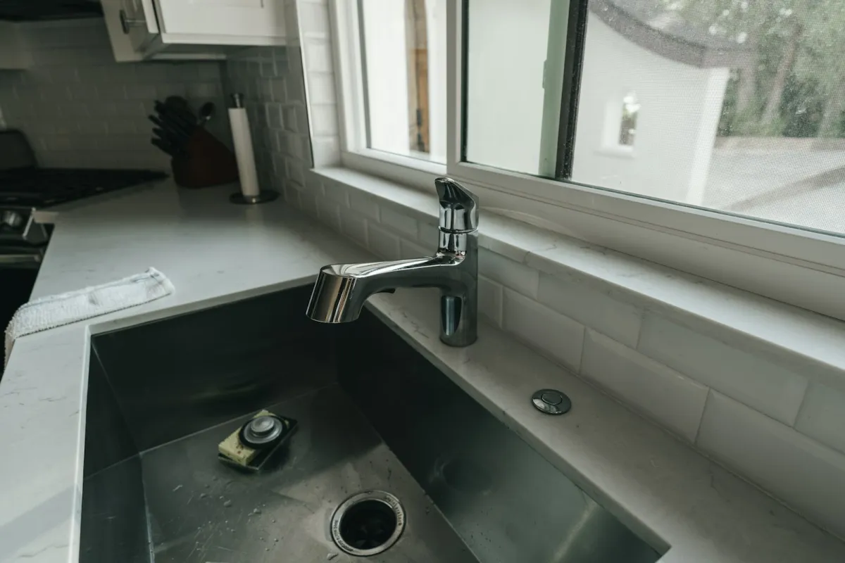 A chrome faucet over a stainless steel kitchen sink by a window