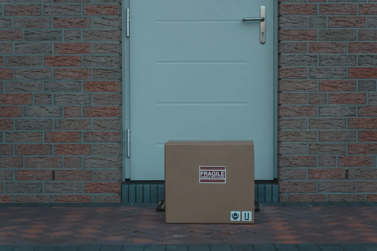 A cardboard box marked fragile left on the ground outside a closed front door in a brick wall A cardboard box marked fragile left on the ground outside a closed front door in a brick wall
