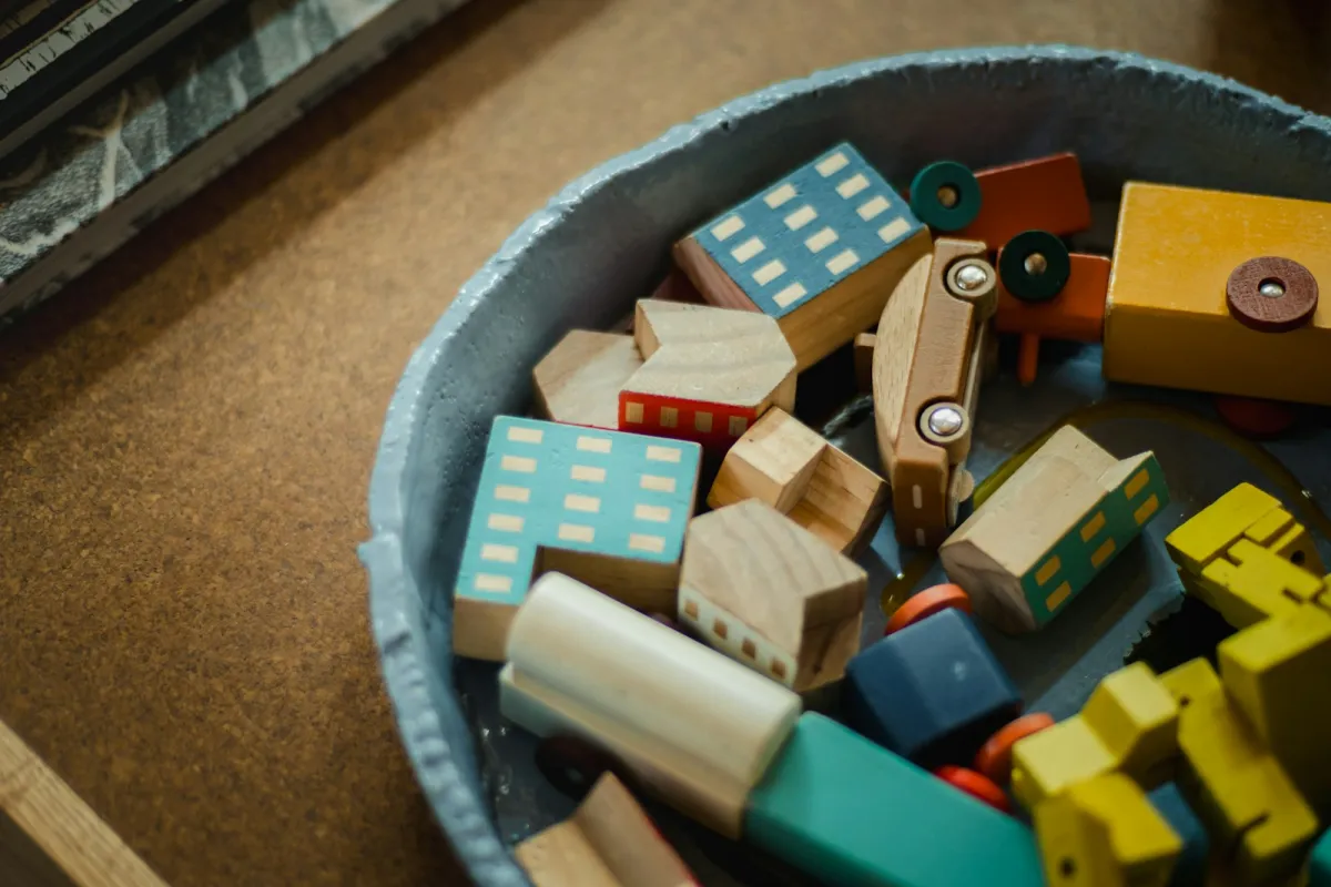 A bowl of colorful wooden toy blocks shaped like houses and cars
