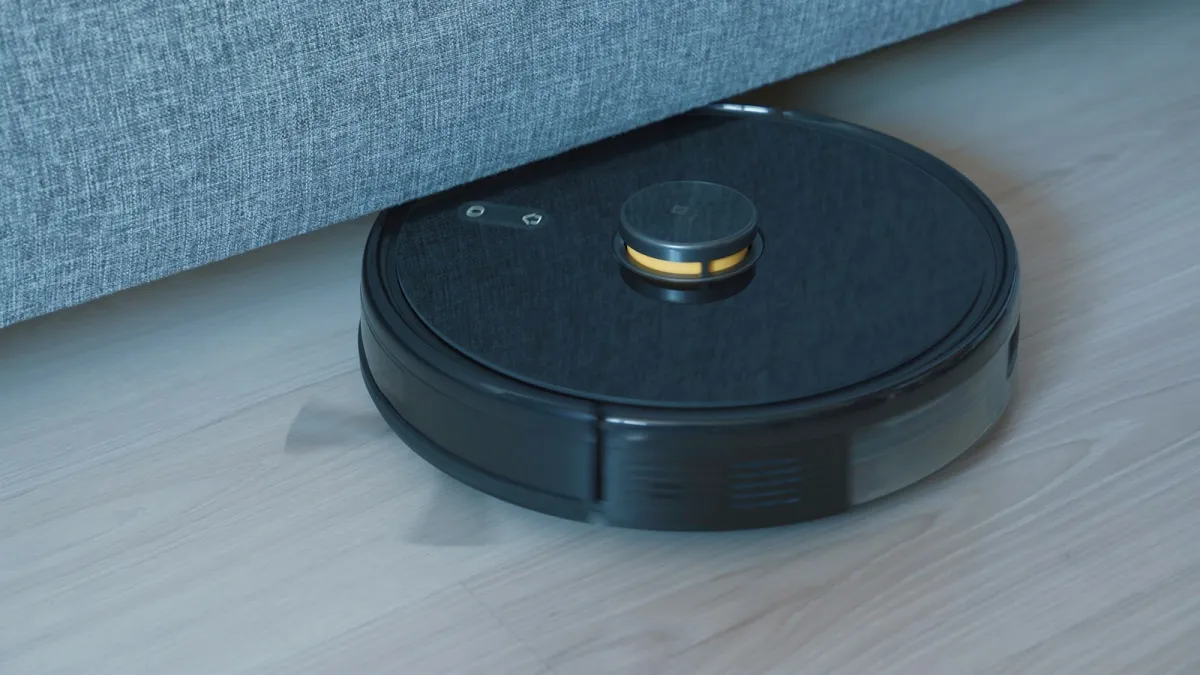 A black robot vacuum cleaning a wooden floor beside a sofa A black robot vacuum cleaning a wooden floor beside a sofa