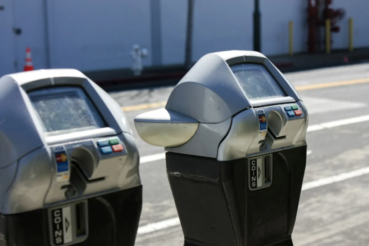Two card-and-coin parking meters on a city sidewalk beside a road Two card-and-coin parking meters on a city sidewalk beside a road