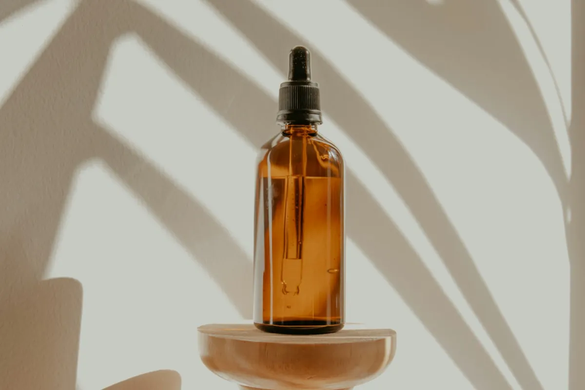An amber glass dropper bottle on a wooden pedestal with palm leaf shadows An amber glass dropper bottle on a wooden pedestal with palm leaf shadows