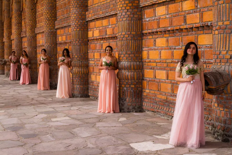 Bridesmaids in long pink dresses holding bouquets along a brick wall