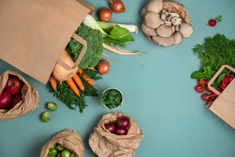 Paper grocery bags spilling over with fresh vegetables on a teal surface
