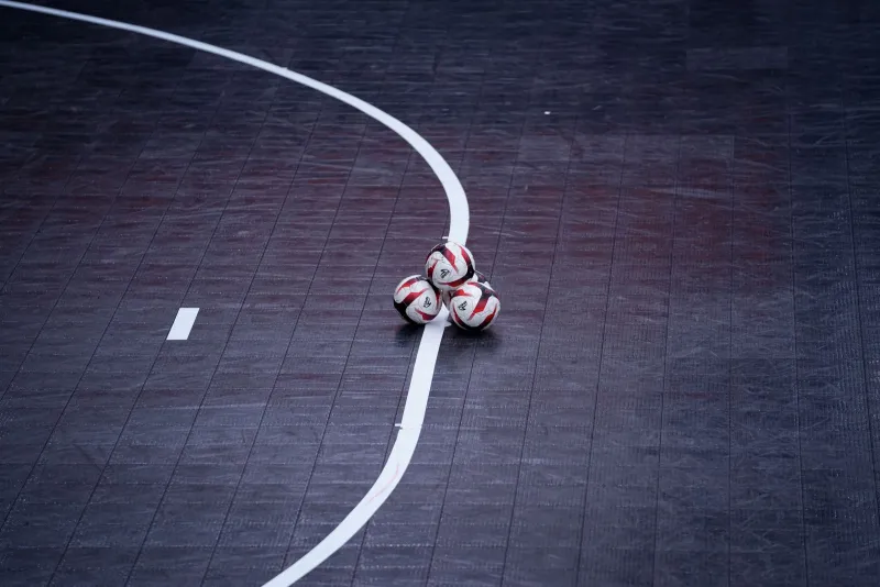 Three futsal balls resting on the line of an indoor court